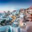 Sunset view of Oia village in Santorini, Greece, with traditional white houses, windmills, and a Greek flag; a top destination for travelers booking an airport taxi transfer.