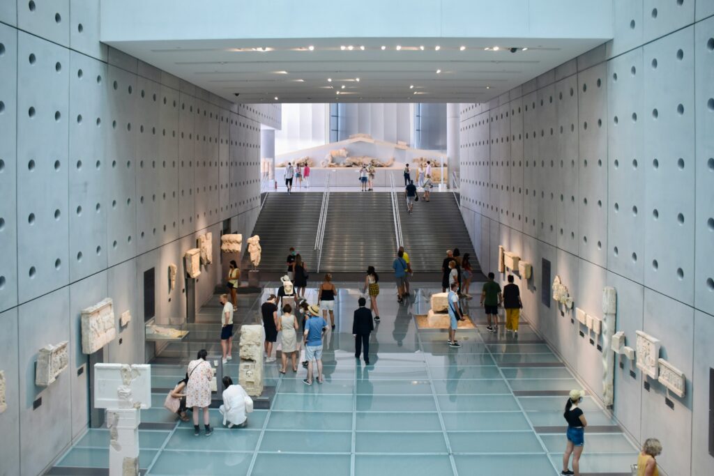Visitors exploring the main gallery of the Acropolis Museum in Athens, surrounded by ancient Greek sculptures and marble artifacts