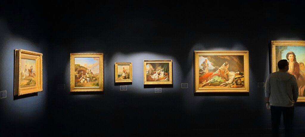 Visitor admiring Greek historical paintings in golden frames at the Benaki Museum in Athens.