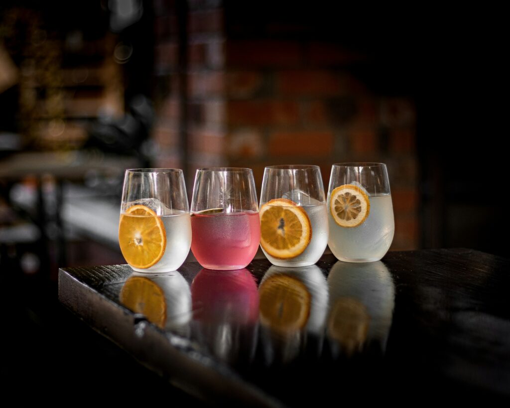 Four cocktails with citrus garnishes lined up on a dark bar counter