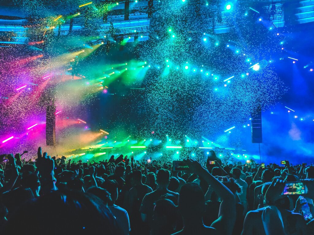 Vibrant electronic dance music festival crowd with bright teal, green, and pink lights illuminating the stage and audience at Tomorrowland.