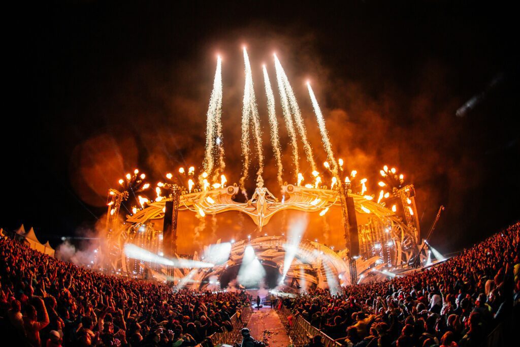 Stunning night view of an EDM festival main stage with golden pyrotechnics, light shows, and thousands of fans cheering at Tomorrowland.