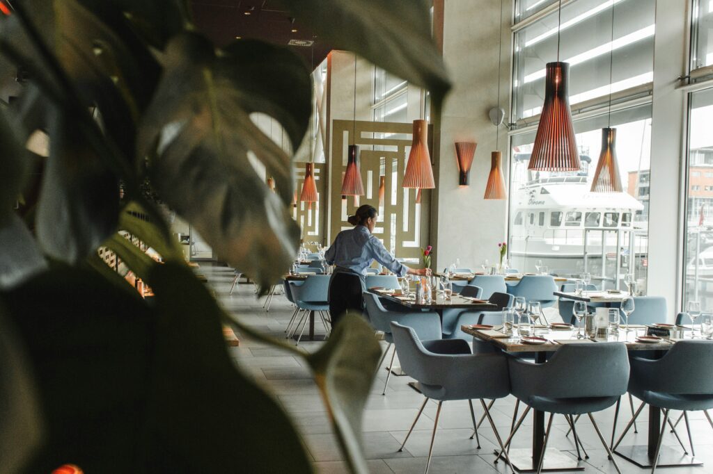 Waitress setting tables in a modern waterfront restaurant with wooden pendant lights