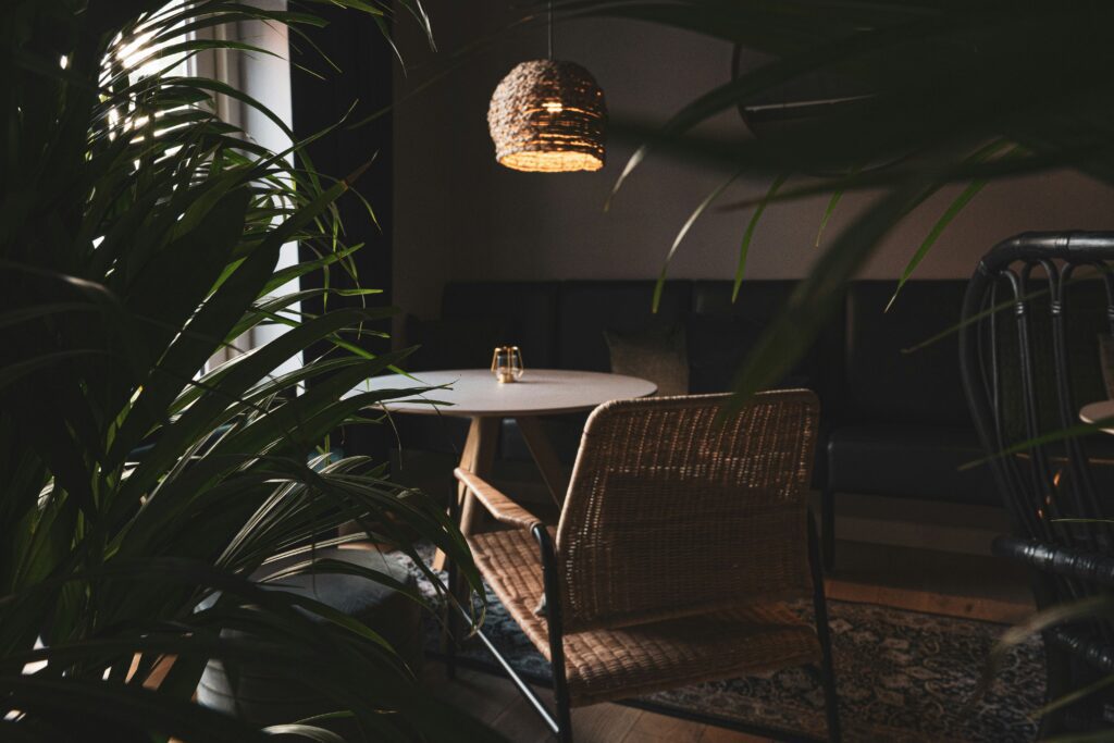 Cozy restaurant interior with rattan chairs, a round table and woven pendant light surrounded by tropical plants
