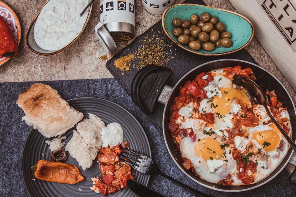 Greek strapatsada with eggs, feta and tomatoes in a pan, served with olives, tzatziki and bread