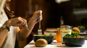 Woman dining at a restaurant with vegetable bowls, bread roll and an iced drink