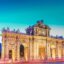 Blurred traffic speeds across the front of Puerta de Alcalá in Madrid at dusk, a popular destination for visitors and locals alike.